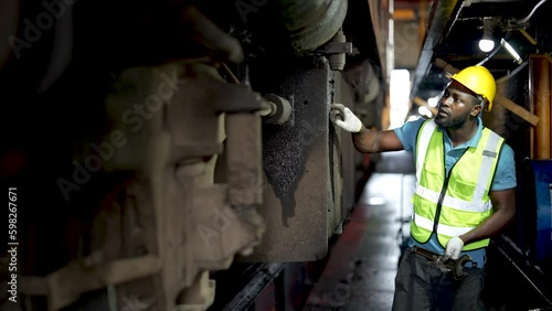 Engineer or maintenance worker repairing and inspecting train undercarriage in workshop.