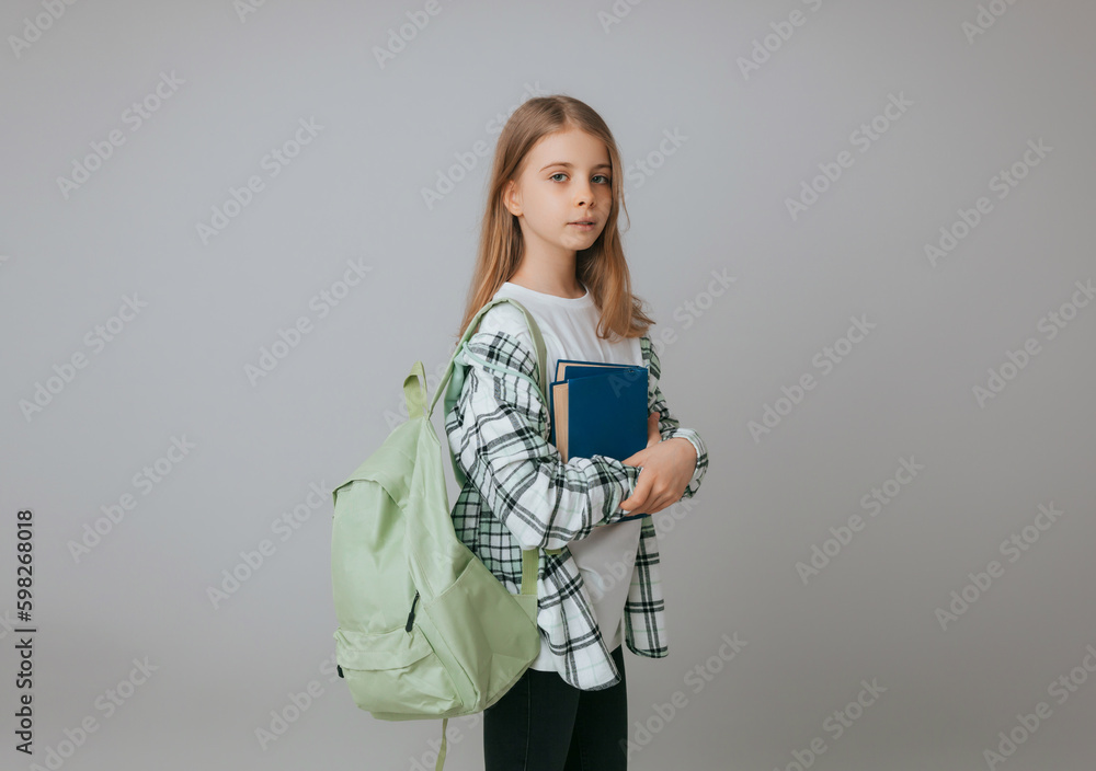 Smiling little schoolgirl 11-13 years old with backpack holding book isolated on gray background studio portrait. The concept of children's lifestyle. Education at school. Smiling little schoolgirl 11-13 years old with backpack holding book isolated on gray background studio portrait. The concept of children's lifestyle. Education at school.