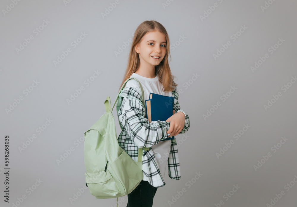 Smiling little schoolgirl 11-13 years old with backpack holding book isolated on gray background studio portrait. The concept of children's lifestyle. Education at school. Smiling little schoolgirl 11-13 years old with backpack holding book isolated on gray background studio portrait. The concept of children's lifestyle. Education at school.