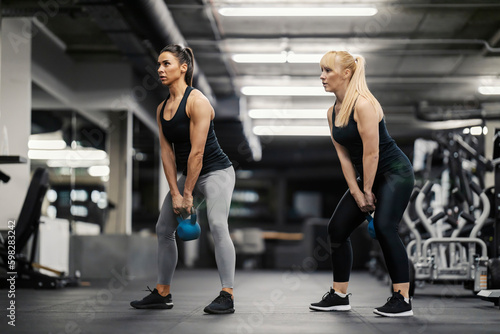Two sportswomen are doing strength training with kettlebells in a gym together.