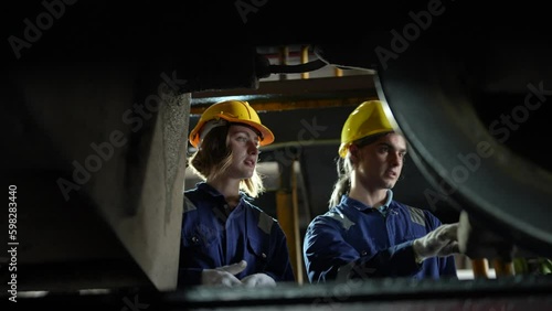 Engineer or maintenance worker repairing and inspecting train undercarriage in workshop.