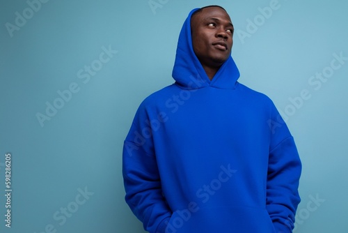stylish cool young guy american with dark skin is dressed in a trendy sweatshirt with a hood on a studio background with copy space