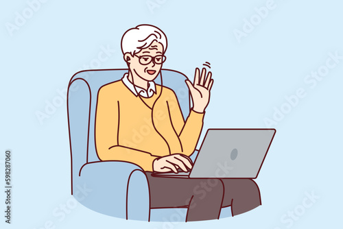 Elderly man makes video call through laptop sitting in chair and waving hand greeting interlocutor. Elderly human with laptop learns computer literacy by participating in online webinar Generative AI