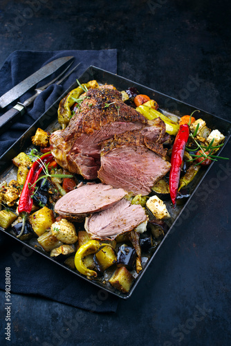 Traditional Greek barbecue leg of lamb with vegetable and feta cheese served as close-up on a rustic tray with copy space
