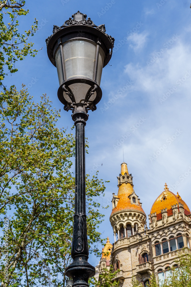 A stunning Barcelona building with a tower and tree in the foreground, illuminated by street lamps. A beautiful representation of Spanish architecture from the past.