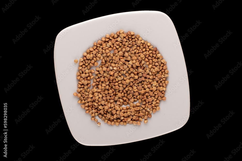 Raw buckwheat with white ceramic saucer isolated on black background, macro, top view. Raw buckwheat with white ceramic saucer isolated on black background, macro, top view.