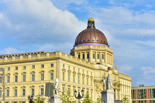 Ancient building with yellow walls, tall windows and a large brown dome on the background of blue sky. Historical architecture and statues. Germany, Berlin, August 2022. © B.inna
