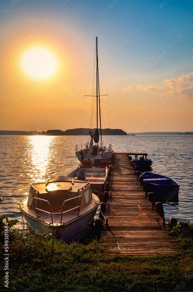 Fototapeta premium Sailing yacht and jetty in the beautiful lake. Empty wooden jetty with moored boats on the lake shore at the sunrise in Mazury region, Poland.