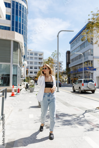 Image of beautiful stylish woman walking on city street on summer day and holding mobile phone. Cyprus, Nicosia