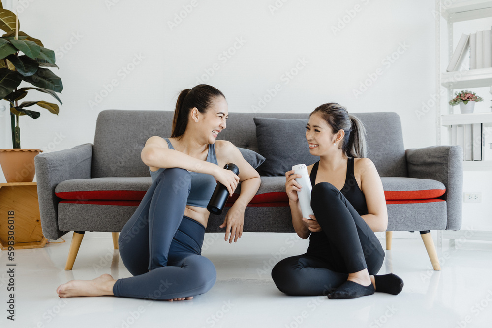 Two young asian women in workout clothes holding water bottles sit smiling, laughing and chatting after exercising. Two young asian women in workout clothes holding water bottles sit smiling, laughing and chatting after exercising.