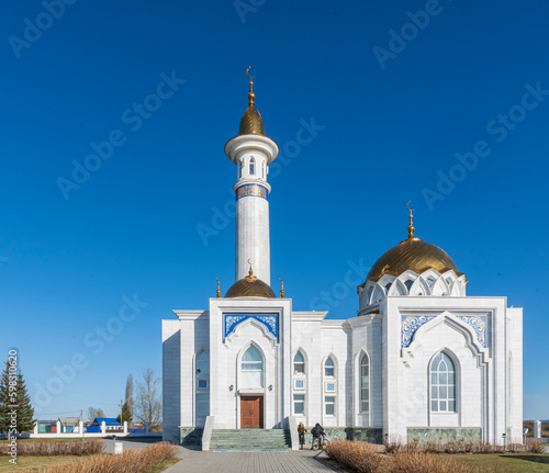 Beautiful Muslim white mosque stands against blue spring sky. There are children at entrance.