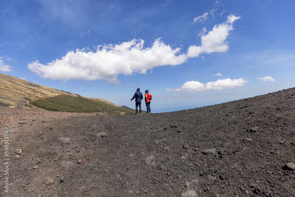 Two people walking the path of the slopes of the volcano Mount Etna, Sicily, Italy.
