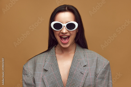 Portrait with beautiful  stylish woman  girl wearing checkered jacket and sunglasses over brown studio background. Bright emotions