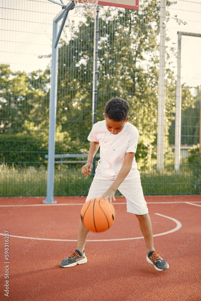 Multiracial boy standing on a basketball court and play with an orange ball Multiracial boy standing on a basketball court and play with an orange ball