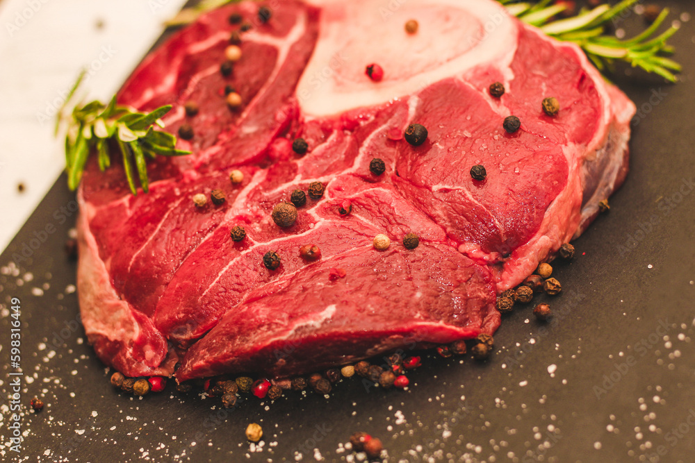 Fresh piece of meat large beef steak on the bone ossobuco with a sprig of rosemary on a black background. Fresh piece of meat large beef steak on the bone ossobuco with a sprig of rosemary on a black background.