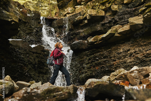 Hiking in mountains. Woman enjoying hike on sunny vacation day. Female with backpack walking close to waterfall. Spending summer vacation close to nature