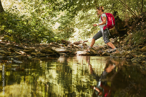 Traveling with backpack concept image. Backpacker female in trekking boots crossing mountain river. Summer vacation trip