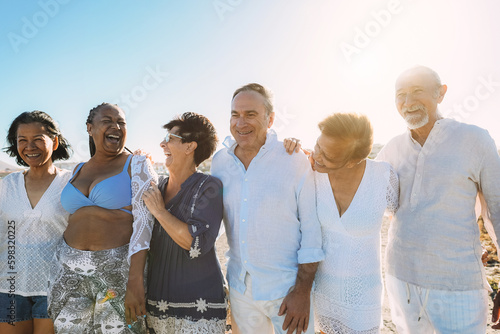 Happy senior people having fun walking on the beach at sunset wearing summer clothes - Joyful elderly lifestyle, vacation and travel concept - Main focus on center friends faces photo