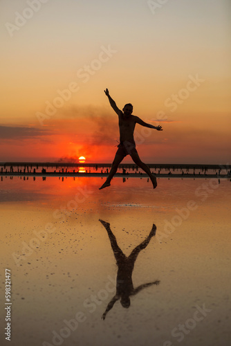 Summer tropic holiday vacation. Silhouette of young man by the sea at sunset having fun jumping enjoying freedom and life. Concept of travel wellbeing, happiness, success. Male reflection on water
