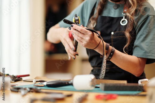 Woman using rotary punch tool for making holes in leather belt