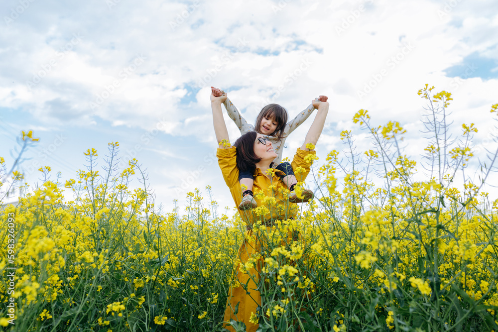 smiling child sitting on mother in the field with yellow flowers smiling child sitting on mother in the field with yellow flowers