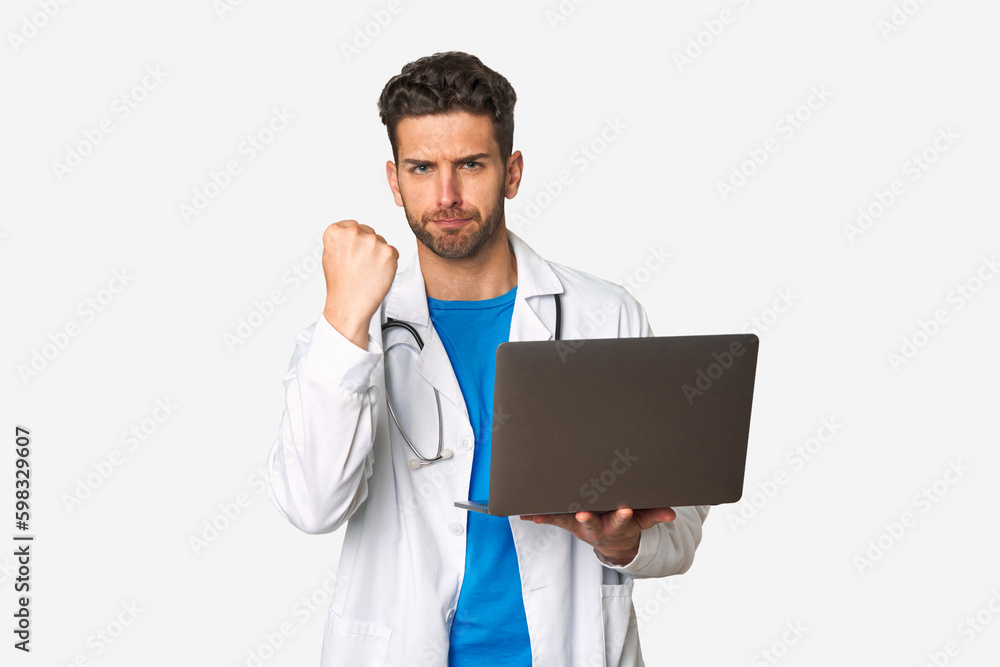 Young doctor man holding a laptop showing fist to camera, aggressive facial expression. Young doctor man holding a laptop showing fist to camera, aggressive facial expression.