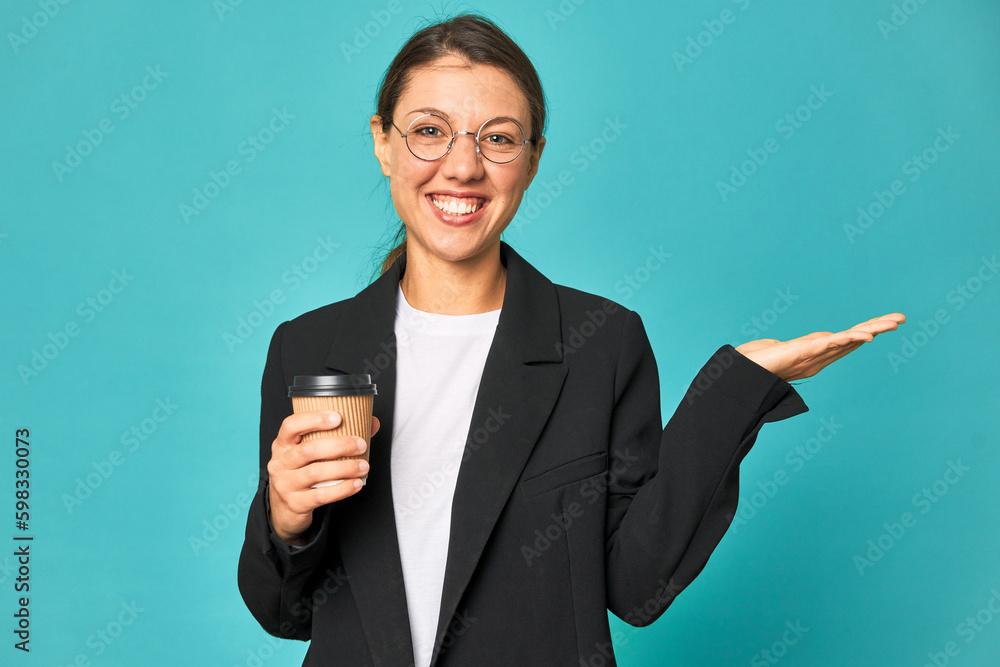 A young caucasian business woman holds a takeaway coffee showing a copy space on a palm and holding another hand on waist. A young caucasian business woman holds a takeaway coffee showing a copy space on a palm and holding another hand on waist.