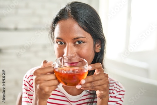 Joyful young Indian woman enjoying a hot cup of tea.