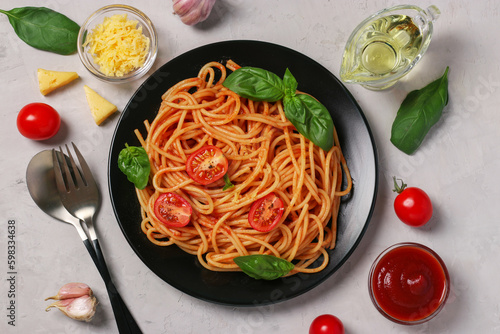 Spaghetti with tomato sauce and cherry tomatoes with basil on black plate on light gray background