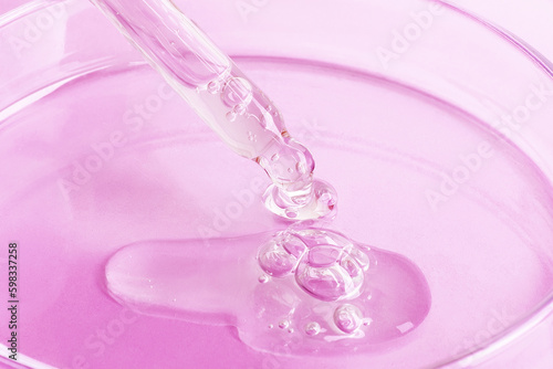 Transparent gel flowing from a pipette into a Petri dish. On a pink background. Close-up.