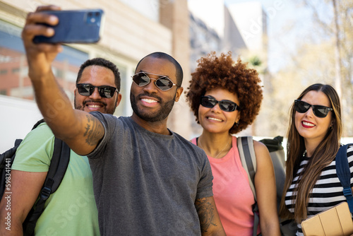 A group of 4 multi-ethnic college students outside the university taking a photo with their mobile phone.Concept of disconnecting from class, sharing photos on social networks, photo of class students