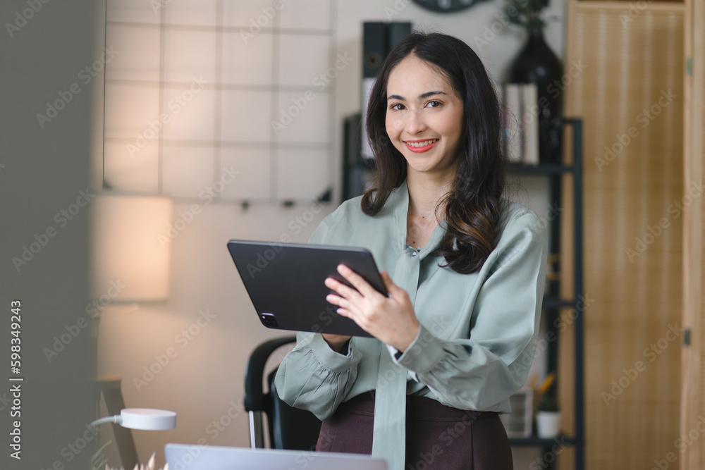 Portrait of a young, cheerful, happy, positive, cute, and beautiful Asian millennial businesswoman standing in her home office with a digital tablet. Portrait of a young, cheerful, happy, positive, cute, and beautiful Asian millennial businesswoman standing in her home office with a digital tablet.