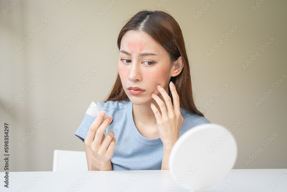 Sensitive skin with cosmetology, Asian young woman looking at red spot on her face from cosmetic allergy in the mirror. Sensitive skin with cosmetology, Asian young woman looking at red spot on her face from cosmetic allergy in the mirror.