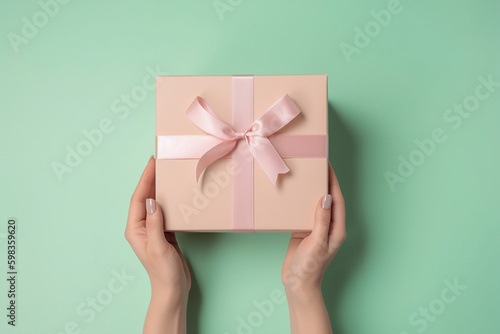 Female hands holding light pink giftbox on the green background. Generative AI