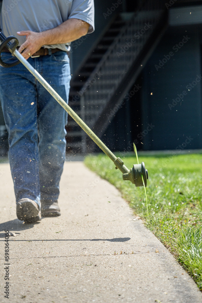 legs of worker with weed eater trimming grass while mowing legs of worker with weed eater trimming grass while mowing