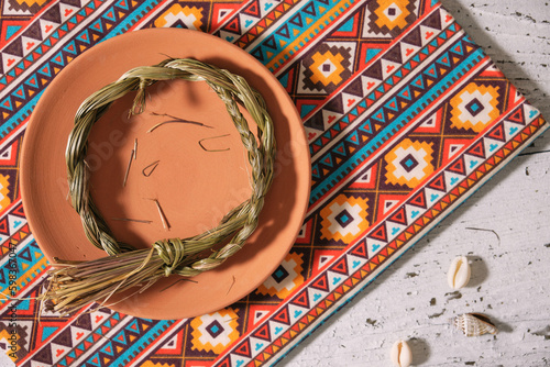 Sweetgrass braid (Hierochloe odorata), also called vanilla grass, on a clay plate, cloth with native american pattern. Overhead view. photo