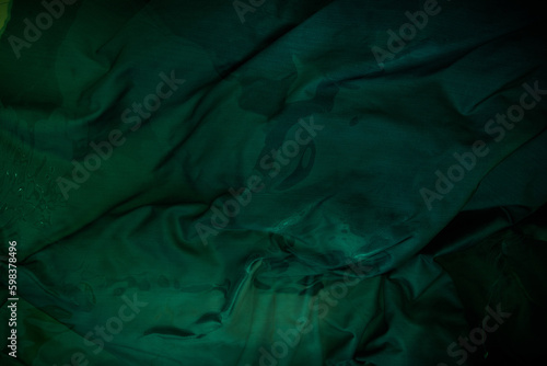 Dark image of a wet green rumpled fabric on the water, with beautiful highlights, for your creative design or illustrations.