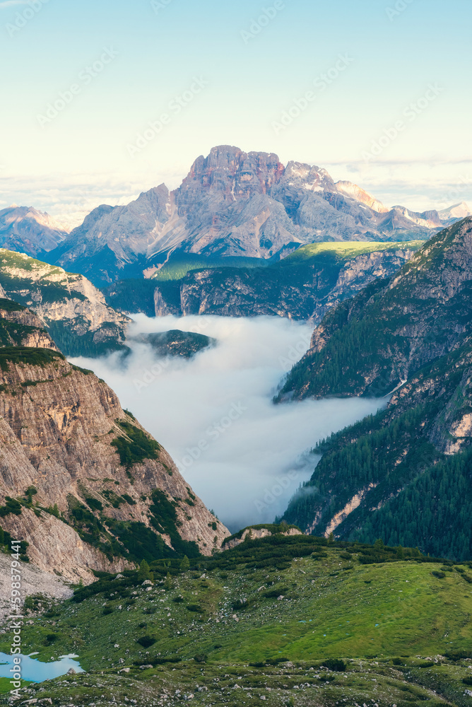 Mountain canyon filled with clouds at sunrise in Dolomites, Alps, Italy. Vertical orientation. Italian mountain landscape