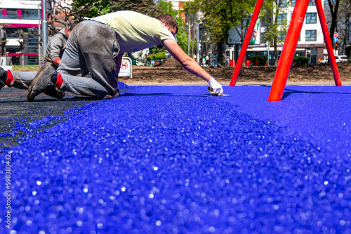 Belgrade, Serbia - April 28, 2023: New childrens playground under construction. A mason hand with trowel  spreading and leveling soft rubber crumbs rubber mulch .for children's playground. photo