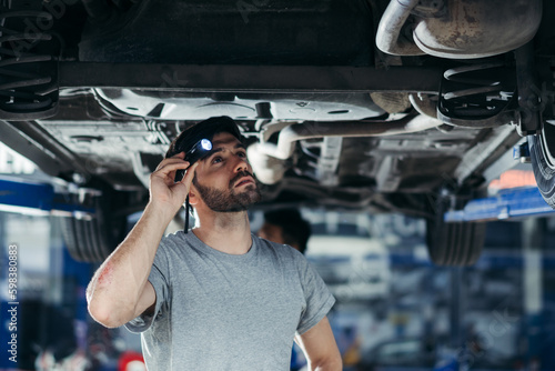 Valokuva automotive mechanic man using flash light checking under car damage at auto repair garage on lifter hoist with assistant