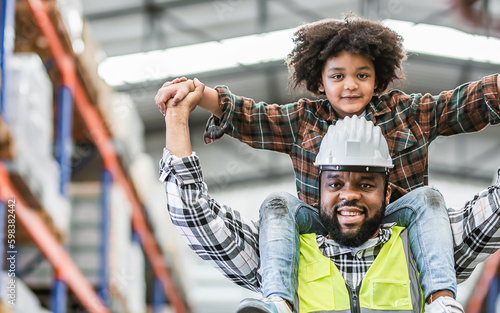 Single African handsome father worker wearing hard hat for safety, carrying his little son on shoulder, working in factory, smiling with happiness and love. Industry, Family, Education, Kid Concept.