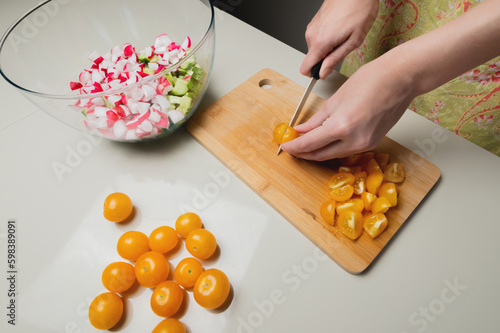 glass bowl stands on the table against the background of hand cutting vegetables with a knife on a wooden board, top view
