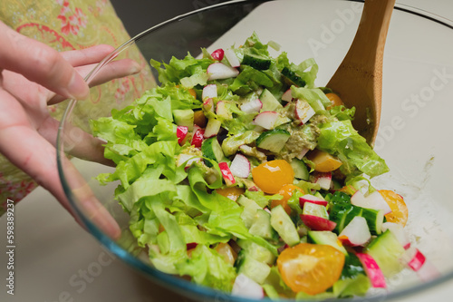 young woman prepares a healthy vegetable salad. Cooking vegetable salad in a glass bowl. Close-up on a table with a wooden spoon