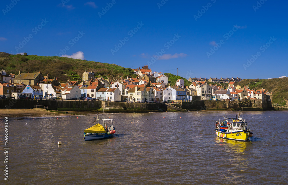 Obraz premium View across the harbour in Staithes at high tide.Two small fishing boats are moored in the middle of the harbour.