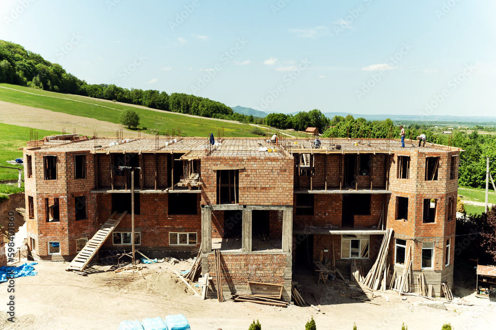the process of building a brick house. builders work on top of the building.roof construction. country cottage under construction the process of building a brick house. builders work on top of the building.roof construction. country cottage under construction