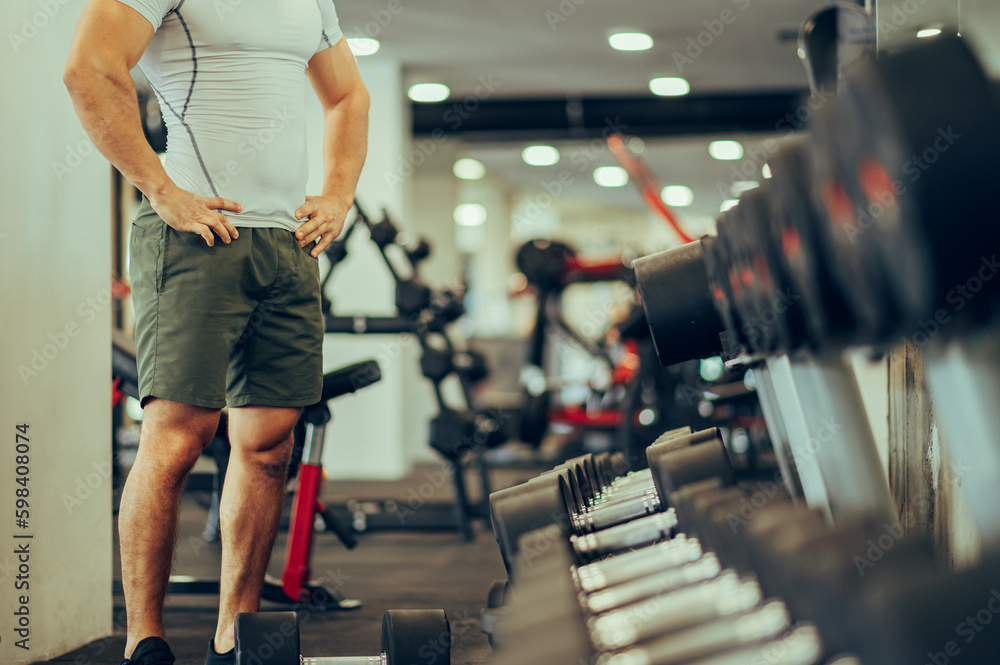 Cropped picture of a bodybuilder's torso and legs with arms on hips in a gym. Cropped picture of a bodybuilder's torso and legs with arms on hips in a gym.