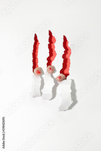 Red nails tearing the white paper from inside, showing red interior. Close up of female fingers, claws conceptual photo.