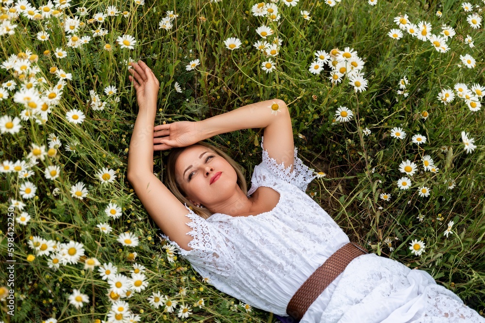 A woman lies in a chamomile field, dressed in a white dress A woman lies in a chamomile field, dressed in a white dress