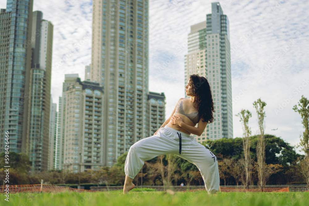young latina woman dancing barefoot in a park with buildings in the background dancing, legs open. copy space