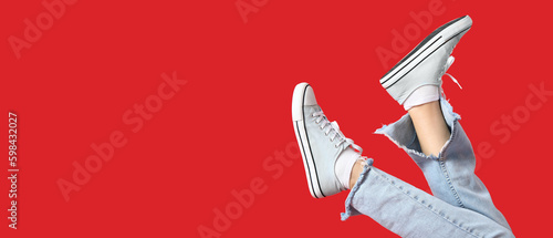 Legs of woman in stylish sneakers on red background with space for text